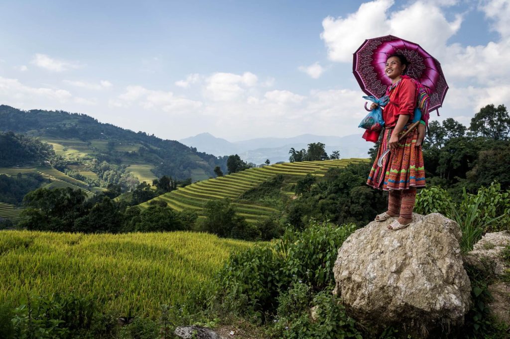 Environmental portrait of a woman in ethnic minority attire standing on a rock above rice terraces in Ha Giang, Vietnam