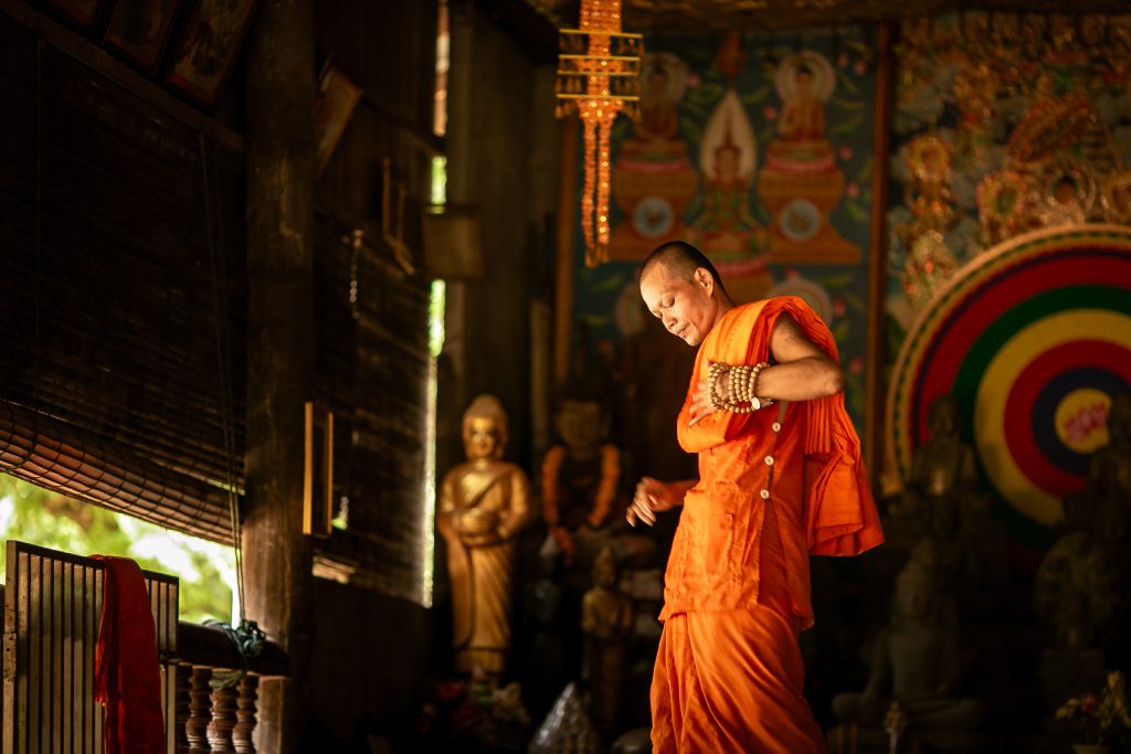 Candid photography of cambodian monk dressed in saffron robe in warm, low light setting.