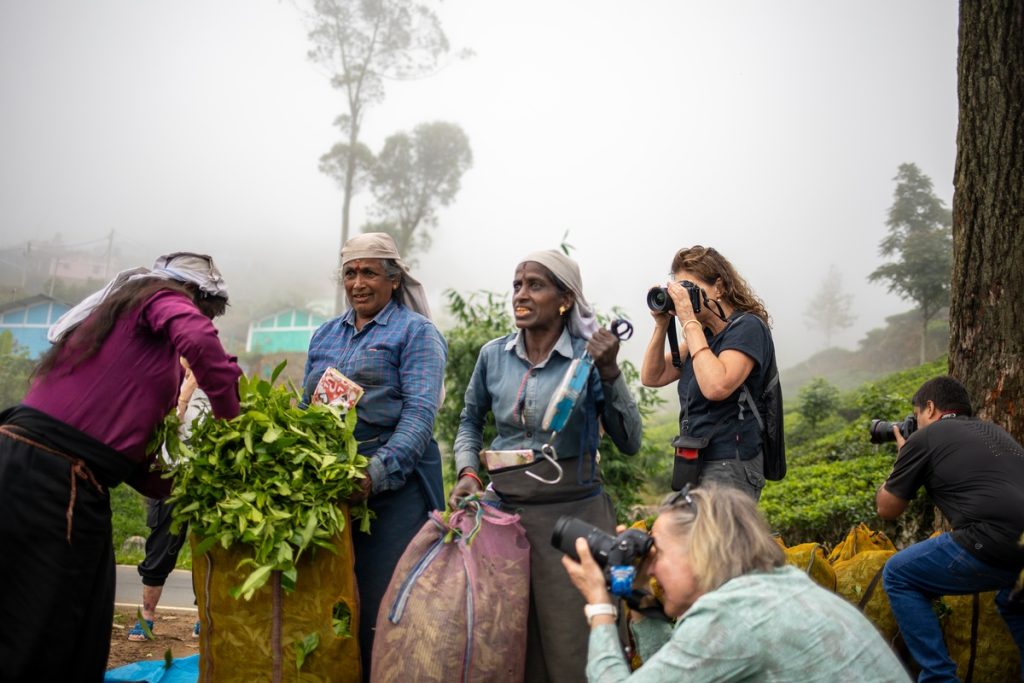 A group of three photographers are working their scenes, while surrounding two local female workers in a tea plantation in Bandarawela, Sri Lanka.